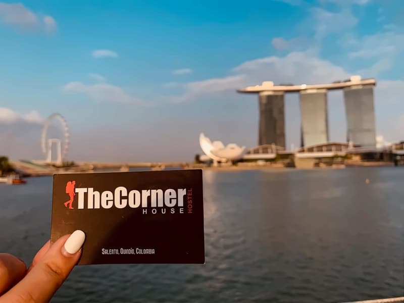 A hand holding a black The Corner House business card in front of Marina Bay Sands, Singapore