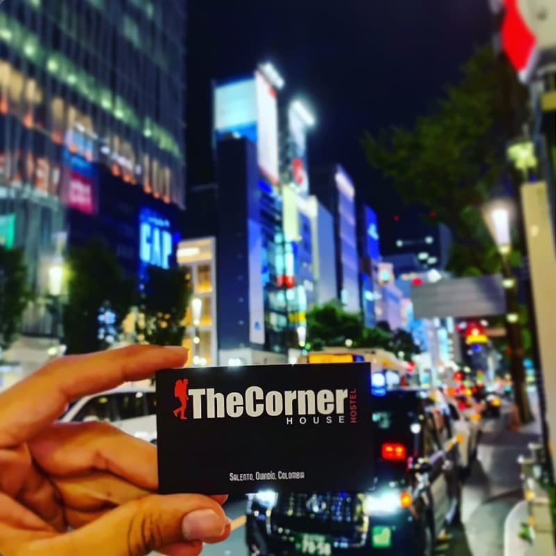 A hand holding The Corner House business card on a neon-lit Tokyo street at night