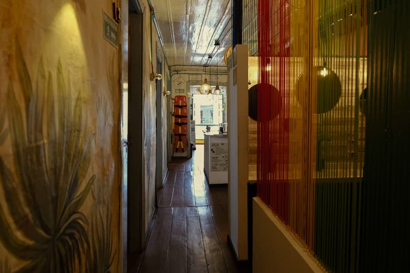 A long wooden-floored corridor with a painted agave on the wall and a rainbow string curtain
