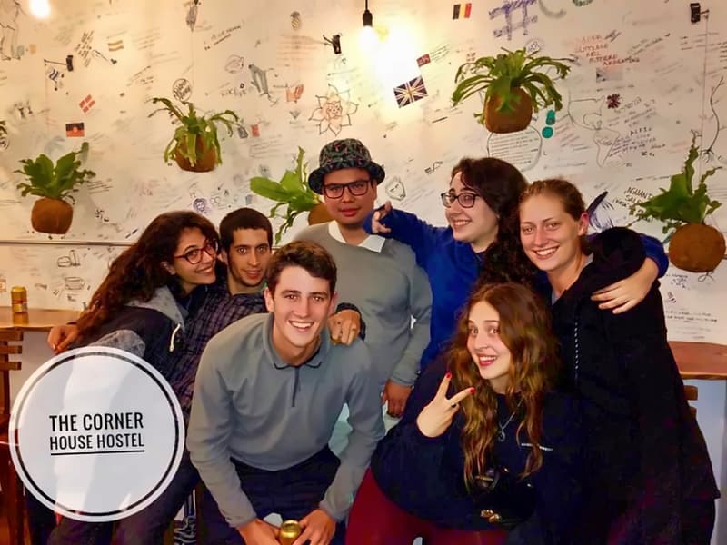 Eight guests crowded together laughing in front of the handwritten wall, one in a patterned bucket hat, another making a peace sign