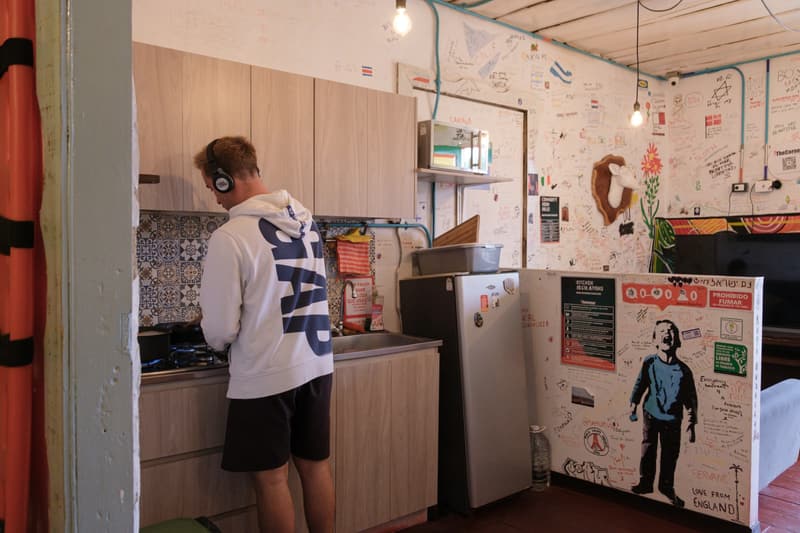 A guest cooking at the stove in the shared kitchen, a small fridge and stencilled artwork on the counter beside him