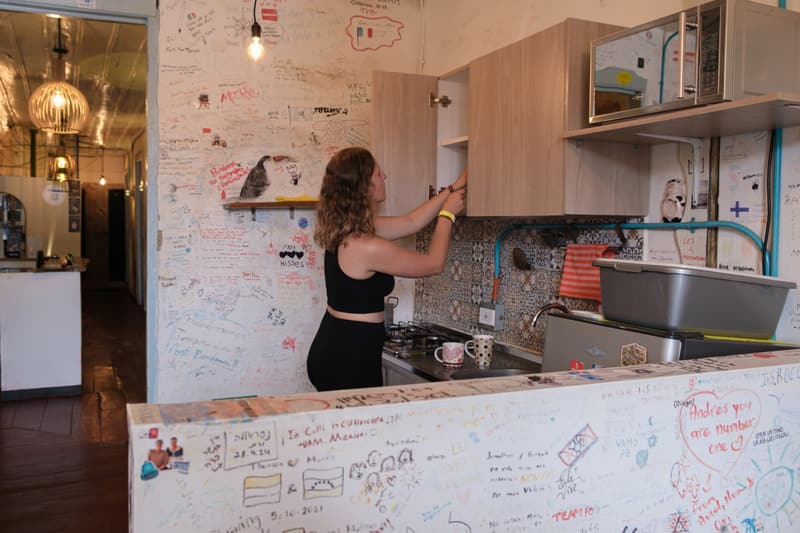 A guest writing on the kitchen wall; compact kitchen with cabinets, microwave and stove, the counter front covered in guests’ messages