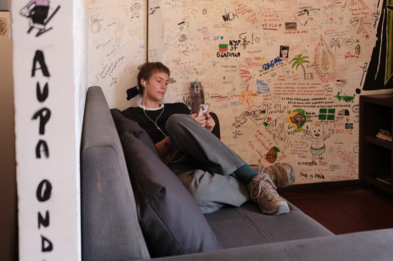 A guest relaxing on a grey sofa with a phone, the wall behind covered in handwriting and doodles