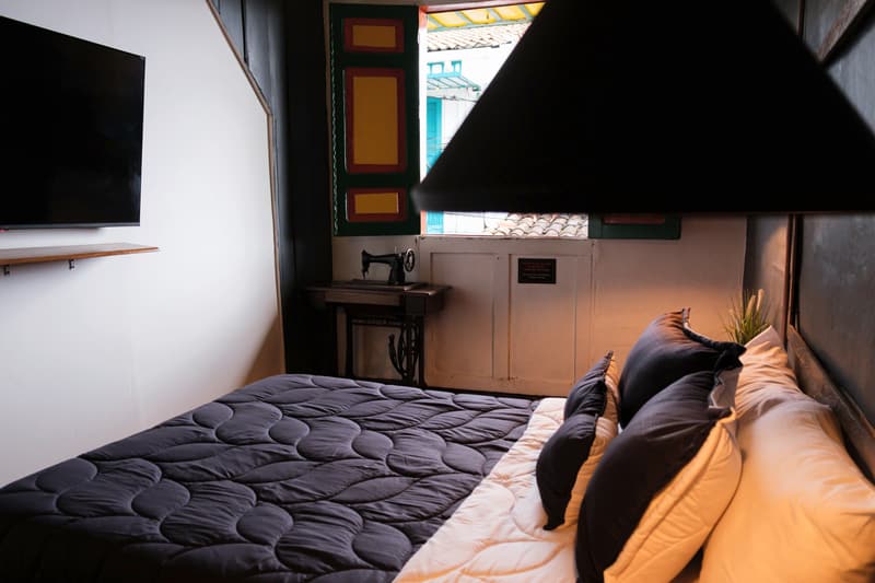 Deluxe Double Room: close view of the bed with orange and black cushions, the TV on the wall and the shuttered window